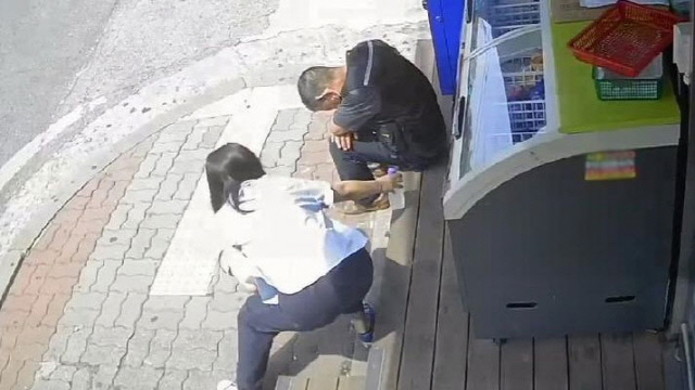 한 여성이 땡볕에 앉아있는 남성에게 물을 건네는 모습. [보배드림 캡처]